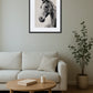 Tableau cheval style estampe noir et blanc au-dessus d’un canapé avec table basse ronde en bois et plante verte