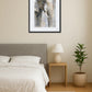 Tableau éléphant abstrait avec effet texture au-dessus d’un lit dans une chambre beige avec table de chevet et plante verte